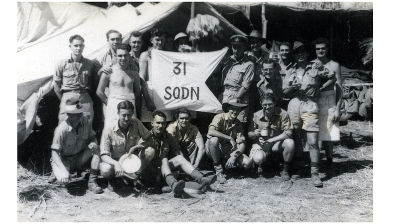 Members of No. 31 Squadron pose at a wartime camp, gathered around a hand‑painted “31 SQDN” sign.