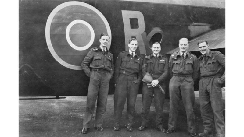 A black and white image of five male military members stand before an aircraft.