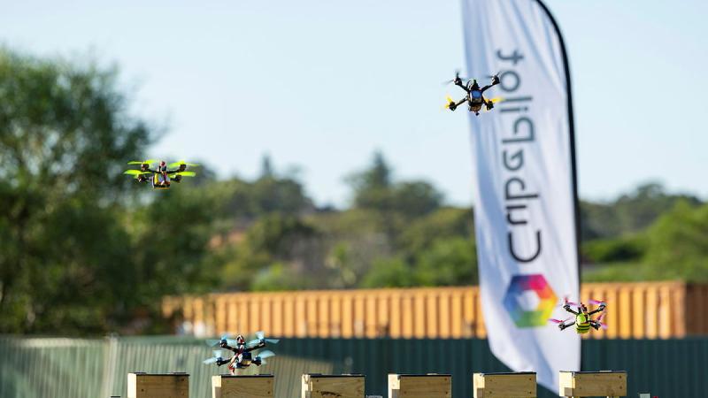 Three drones are racing across a field towards the camera.