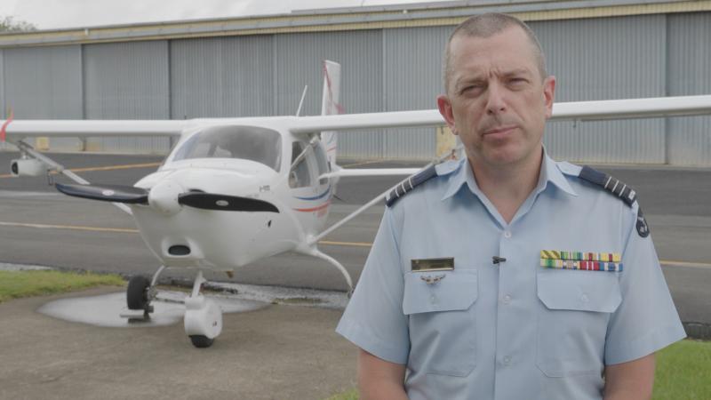 A man in uniform standing next to a small white aircraft.