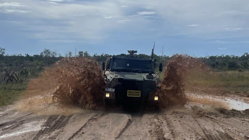 Mud splashes the side of an Army vehicle as it drive on a wet, dirt road.