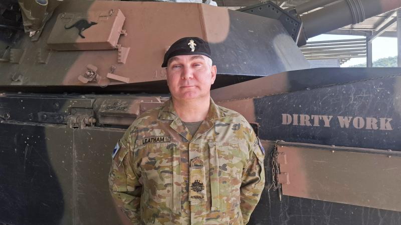 An Army major stands in front of a tank and faces the camera.