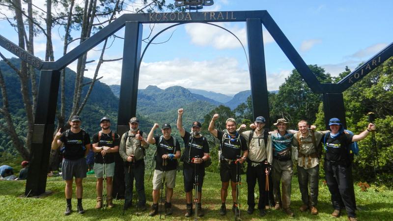 Royal Australian Air Force personnel wearing hiking kit, stand in front of the Ower’s Corner Kokoda Track monument for a group photo.