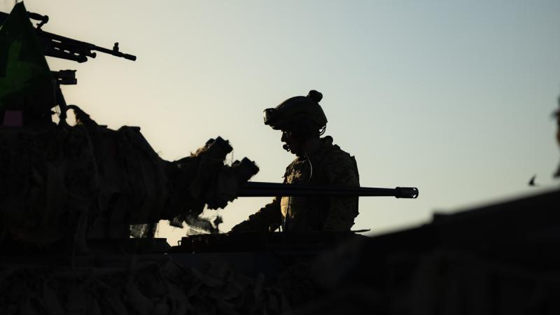 A silhouette of a soldier with an Army vehicle with a large gun on it.