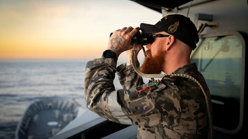 A sailor uses binoculars to look out to sea.