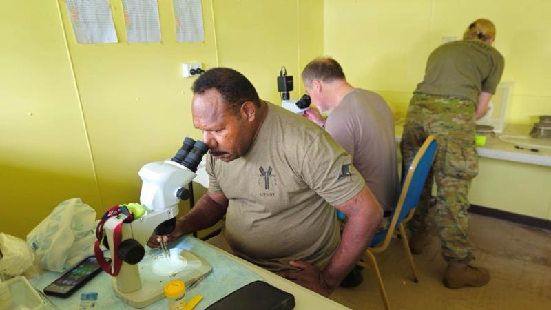 A Papua New Guinea sergeant looks down a microscope to inspect mosquiotoes