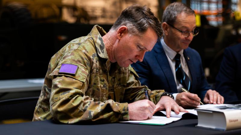 Two men sit at a table signing documents.