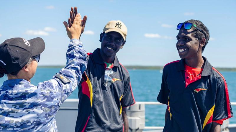 A Navy member gives a high five to an Arnhem Land student as another watches and smiles. 