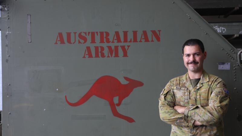 A man in uniform stands beside a large metal panel marked with the words Australian Army and a red kangaroo stencil.