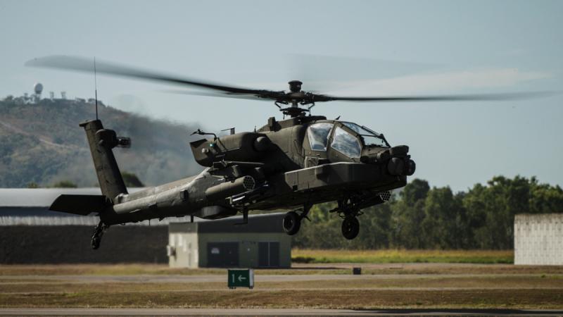 A black military helicopter takes off from the tarmac at an airport.