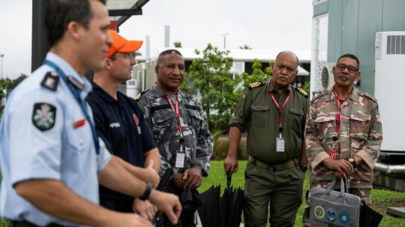 A detective in blue uniform addresses a small group of people outdoors.