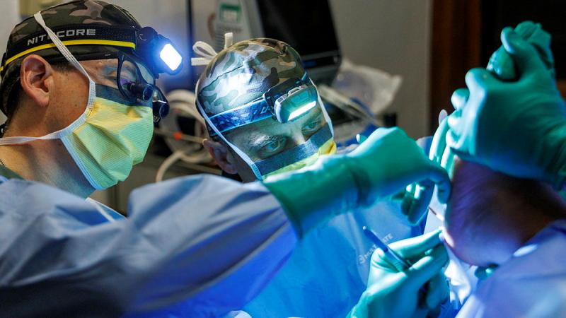 Two Army medical staff perform surgery under bright lights.