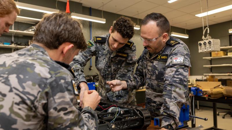 People in uniform gathered around a table working on a device.