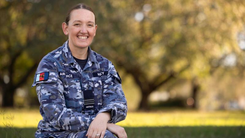 A woman in uniform sitting outdoors, smiling.