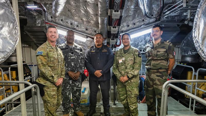 Defence and policing personnel from various nations stand inside a patrol boat.