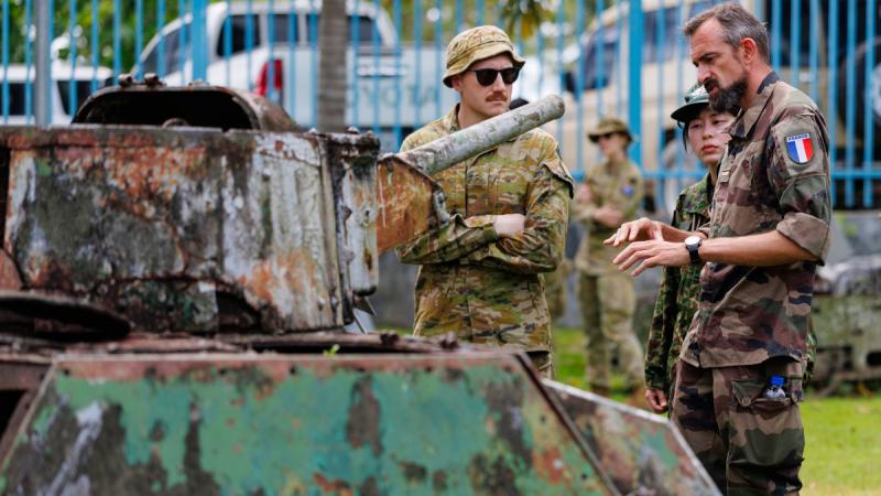 People in uniform talk next to a rusted armoured vehicle.