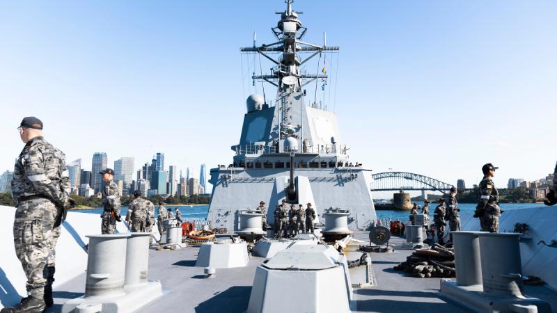 The bow of a Navy ship faces the camera as sailors man the deck on all sides.