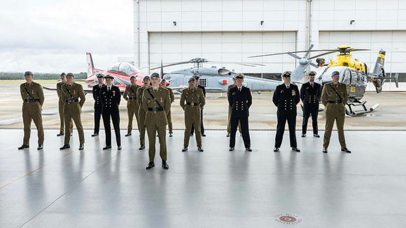 A group of military personnel standing inside an aircraft hangar.