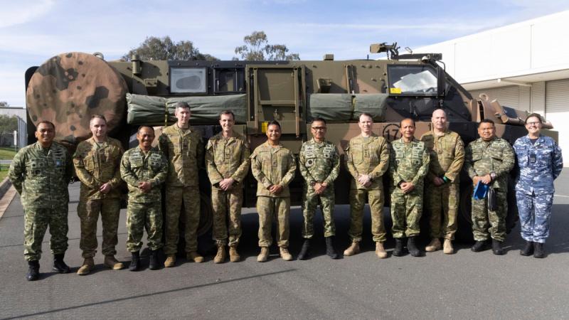 A group of people standing in front of a large Army truck.