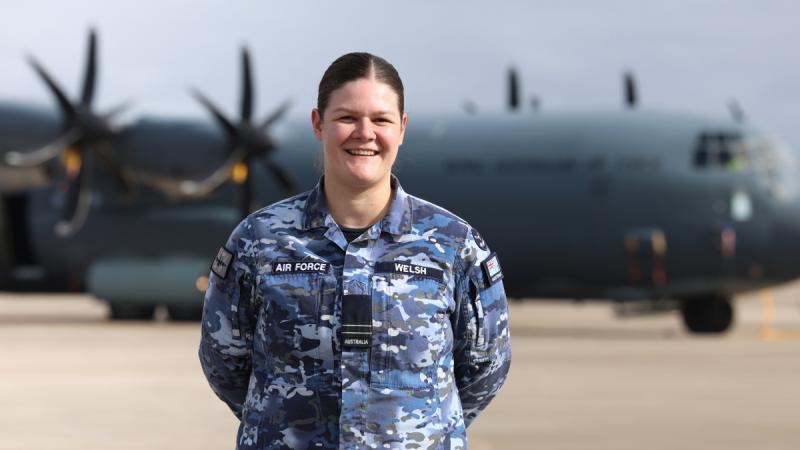 A woman in Air Force uniform stands on a tarmac in front of an aircraft.