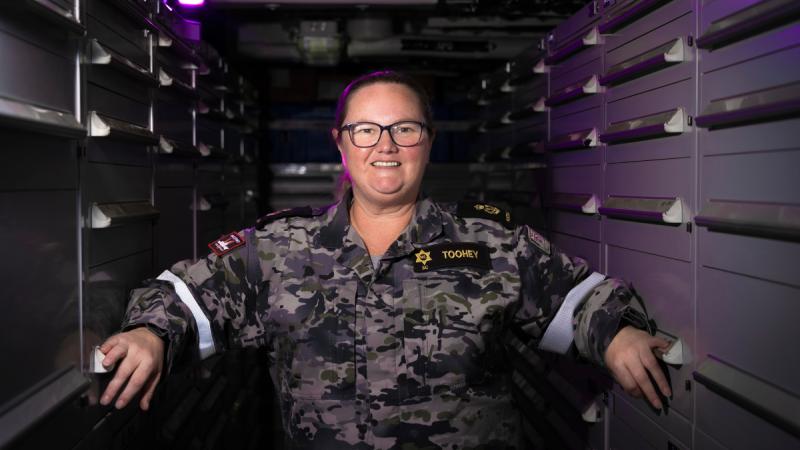 A woman in Navy uniform in the store room of a ship.