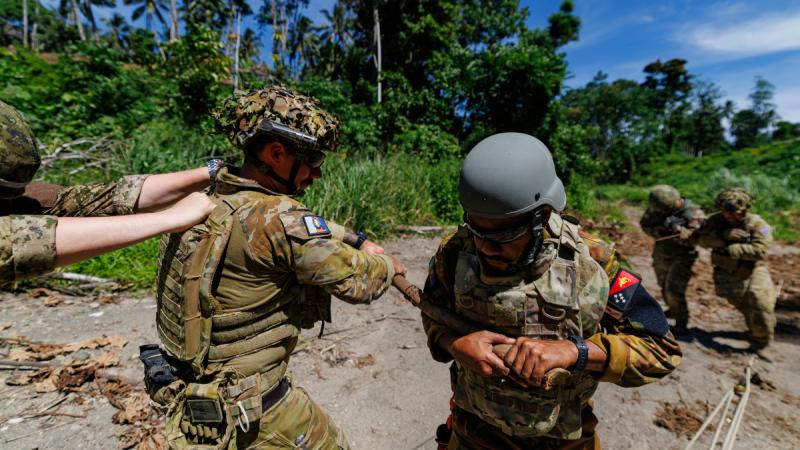 Military personnel hold on to poles and ropes.