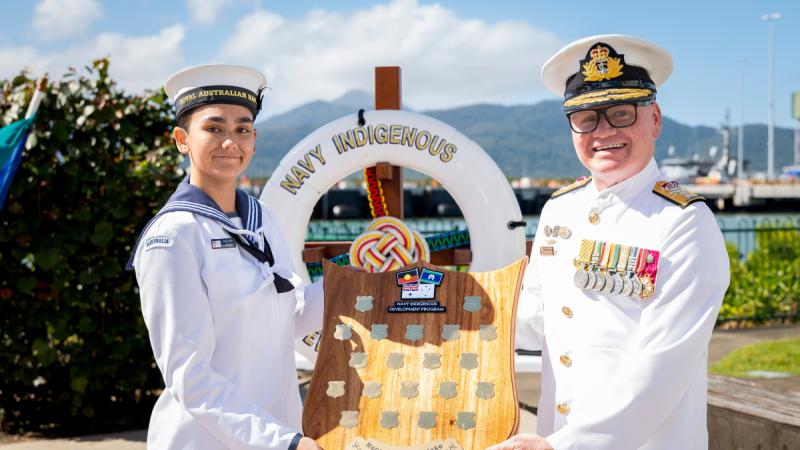 Two Navy officers hold an award and face the camera smiling.