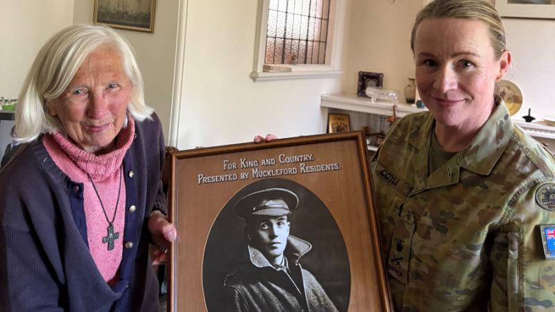 An elderly woman and a woman in Army uniform hold up a black-and-white portrait photo of a military man.