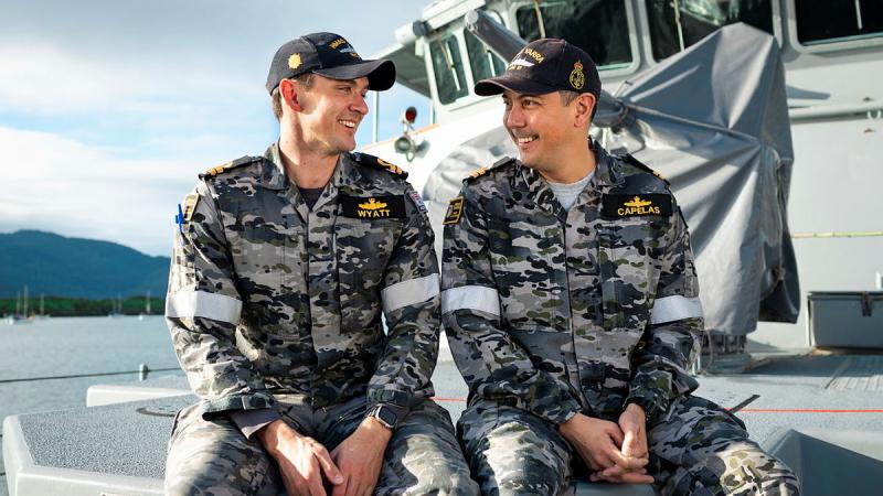 Two Navy officers sit on the forecastle of a ship and enjoy a laugh.