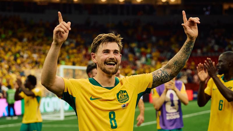 An Australian soccer player has his arms in the air after scoring a goal.