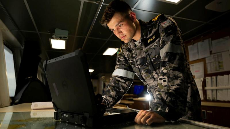 A Navy officer looks down at some new technology as he makes plans for his ship.