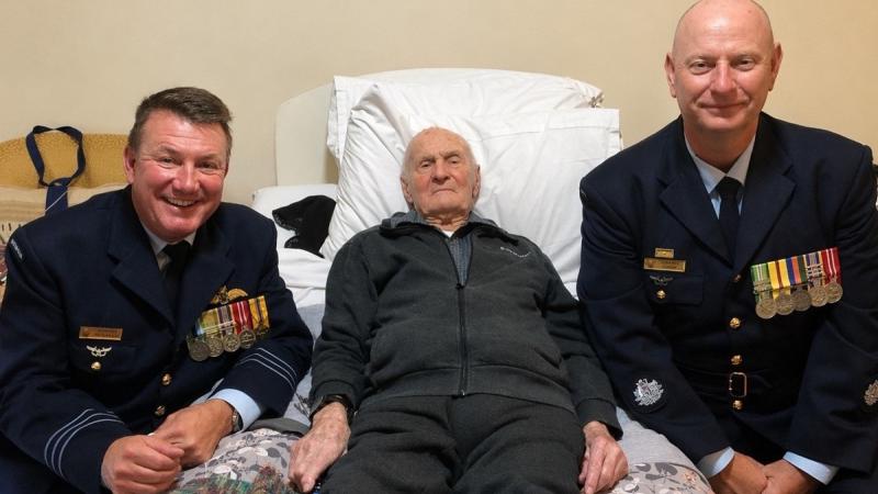 Two men in Air Force uniform sit with an elderly man lying in a bed.