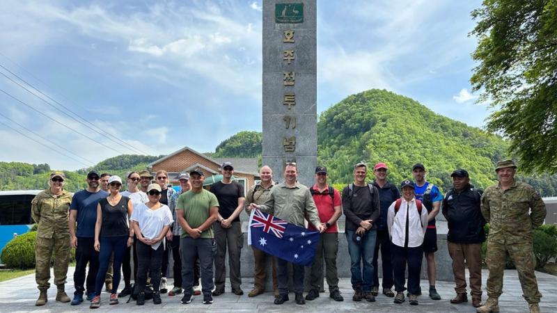 A group of people standing in front of a large stone monument, with the person in the centre holding an Australian flag.