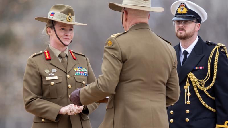 A female Army officer accepts a handover plaque from a male Army officer.