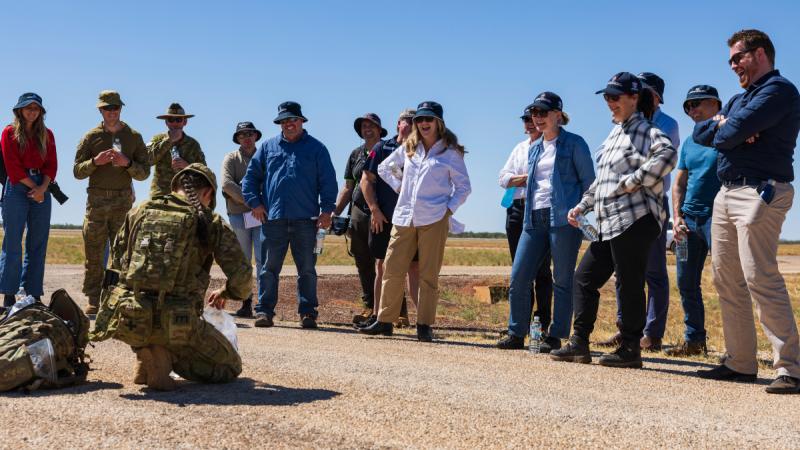 A group of people gathered around and Army member showing contents of a ration pack.