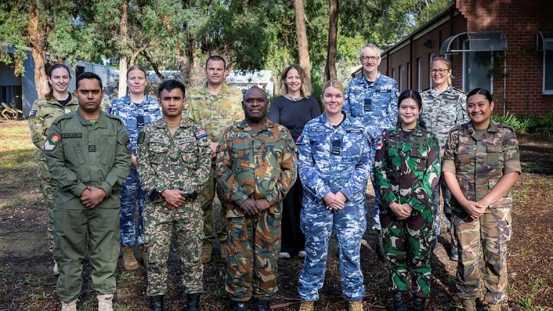 Australian military and regional partner military public affairs specialists face the camera and smile.