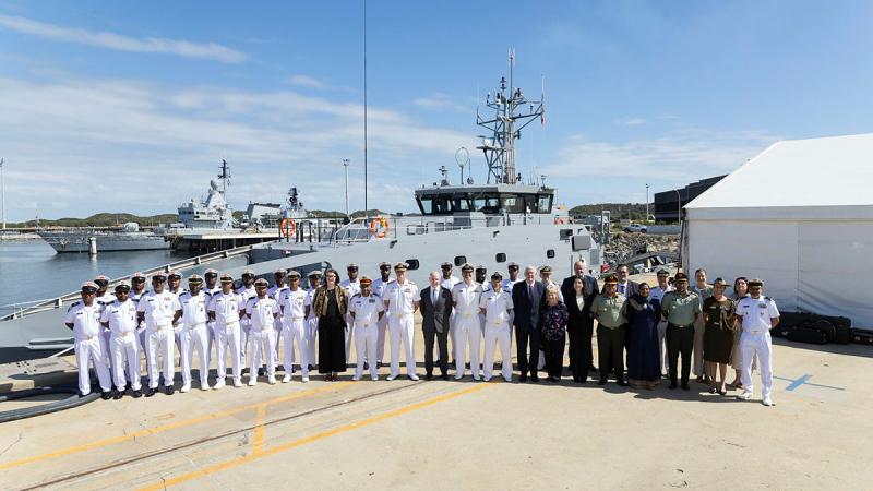 A large group of people in uniform stand in front of a patrol boat.