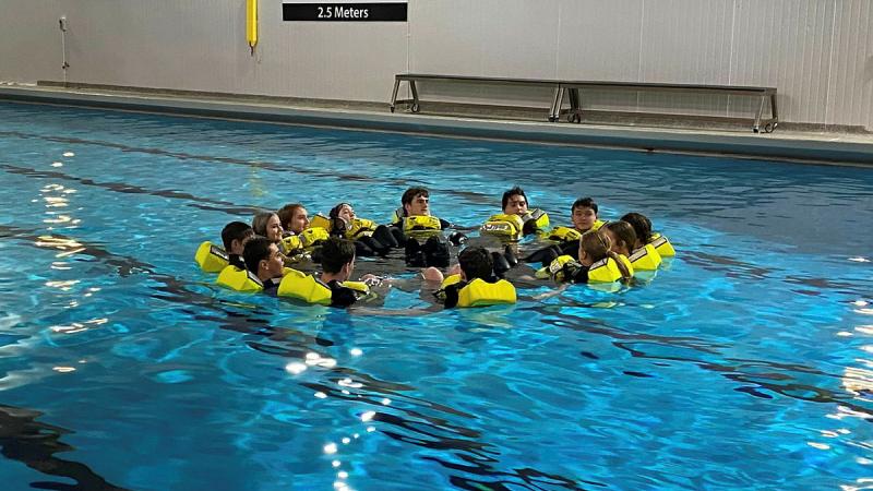 Teenagers wearing buoyancy attire form a circle in a pool.