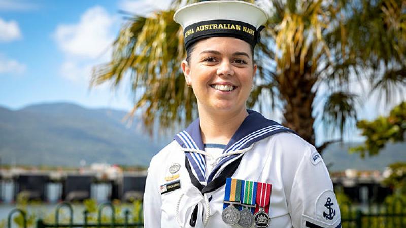 A female sailor smiles for a portrait photo in front of a palm tree.