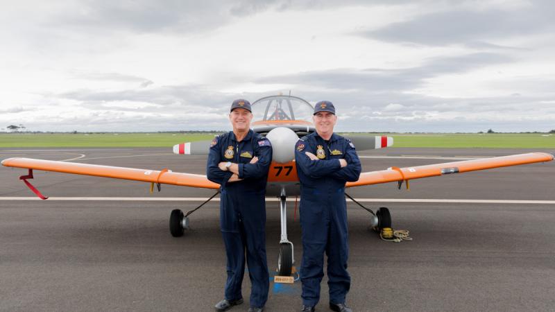 Two Air Force officers stand in front of a turbo prop aircraft and face the camera.