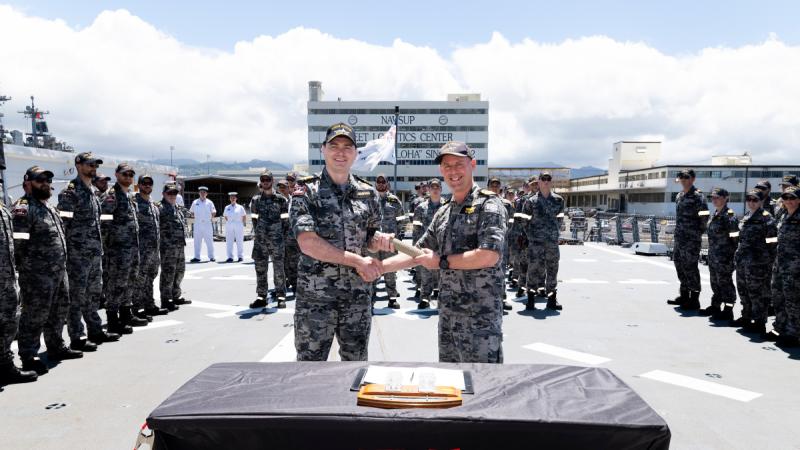 Two Navy officers shake hands as they hand over responsibility for HMAS Sydney