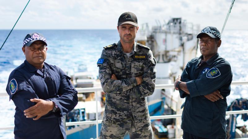 Three men in uniform standing on the deck of a ship with their arms crossed.