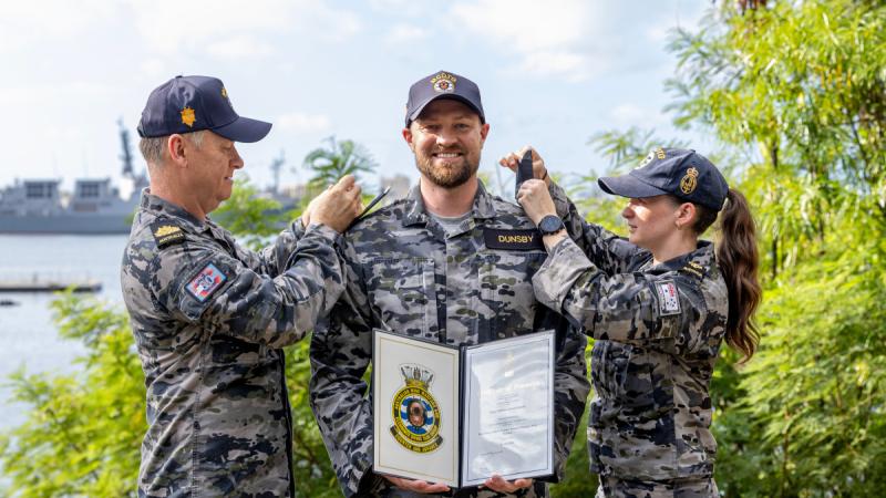 A man and women attach new rank slides to the shoulders of another man holding a certificate.