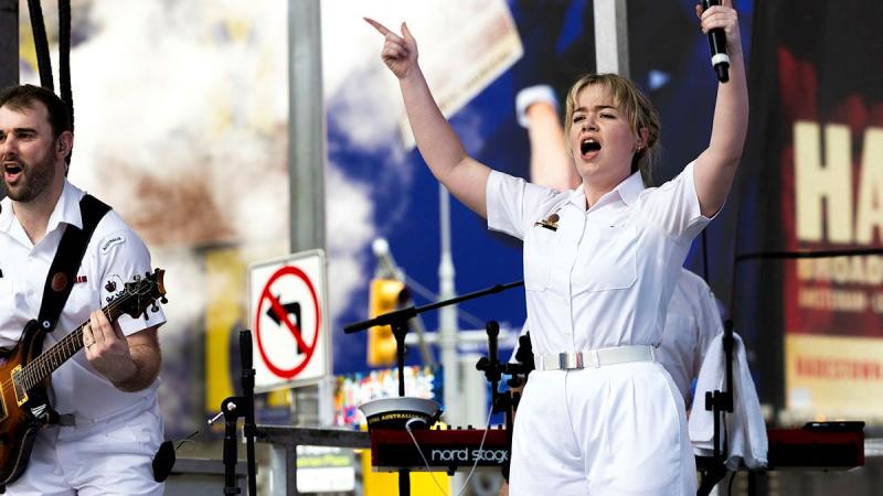 A Navy singer holds her hands in the air to encourage a crowd to sing along.