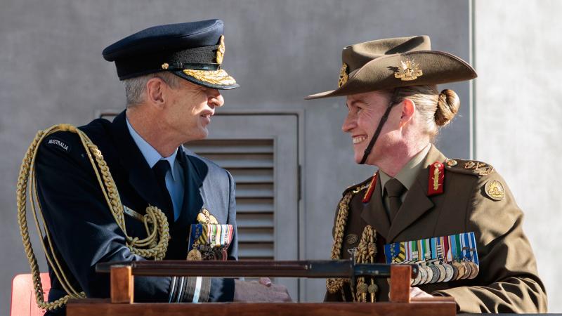 A man and a woman in military uniform shake hands behind a podium.