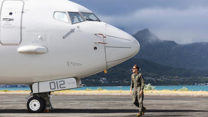 Flight Lieutenant Oscar Borton stands on the tarmac in front of a P-8A Poseidon conducting a pre-flight check prior to a mission at Marine Corps Base Hawaii.