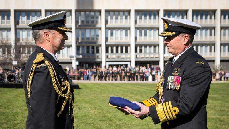 A man hands a folded flag to another man.