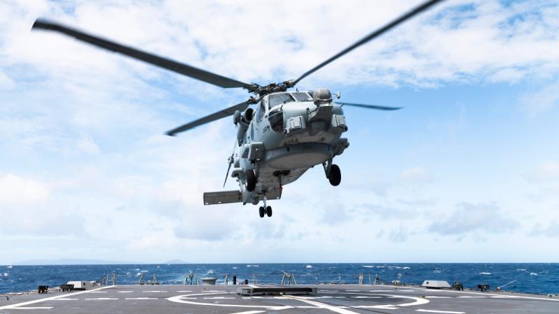 A helicopter hovers above a ship flight deck.