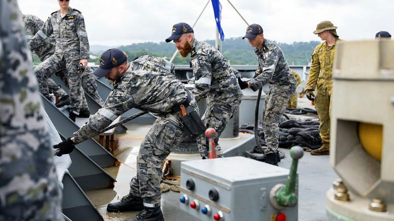 Navy personnel pull on ropes on the deck of a ship.