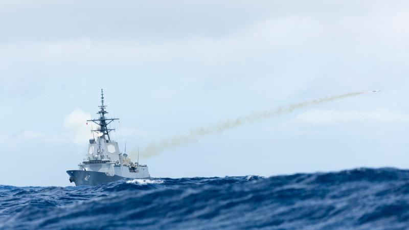 A missile launches from a warship at sea.